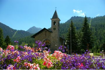 L'immagine rappresenta la chiesa parrocchiale di Claviere attorniata da fiori nel periodo estivo